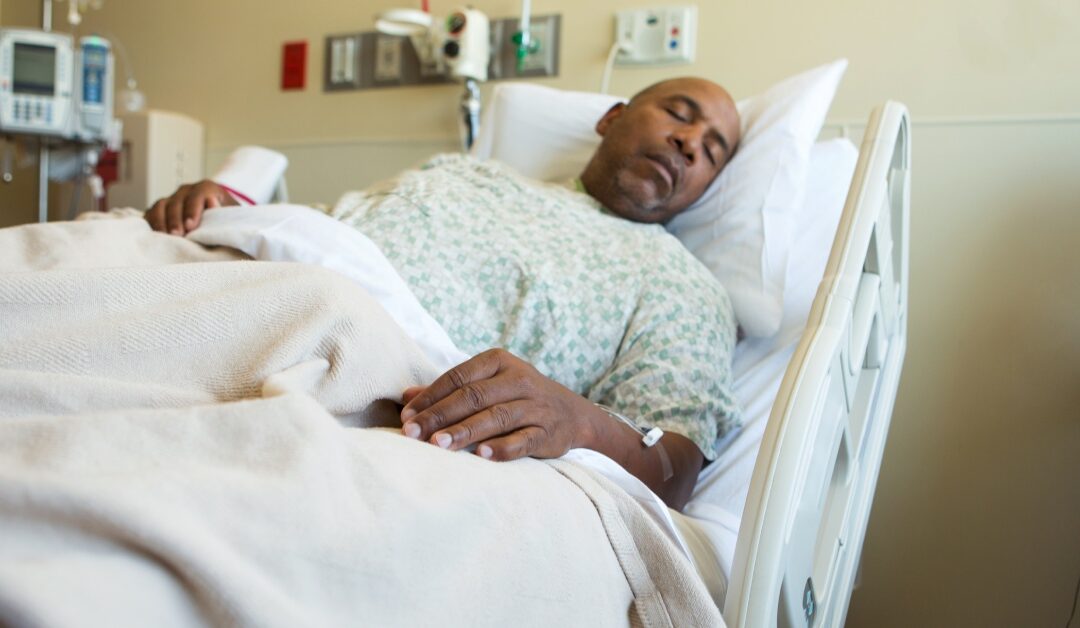 A patient in a hospital bed sleeping with a neutral expression on his face. The bed's backrest is elevated at about 45 degrees.