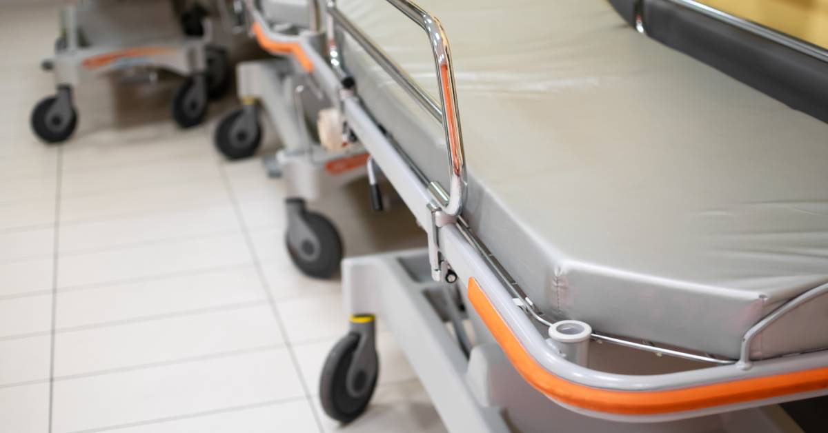 Close-up of an empty medical stretcher. The stretcher's metal handrails shine, and its mattress and frame are clean.